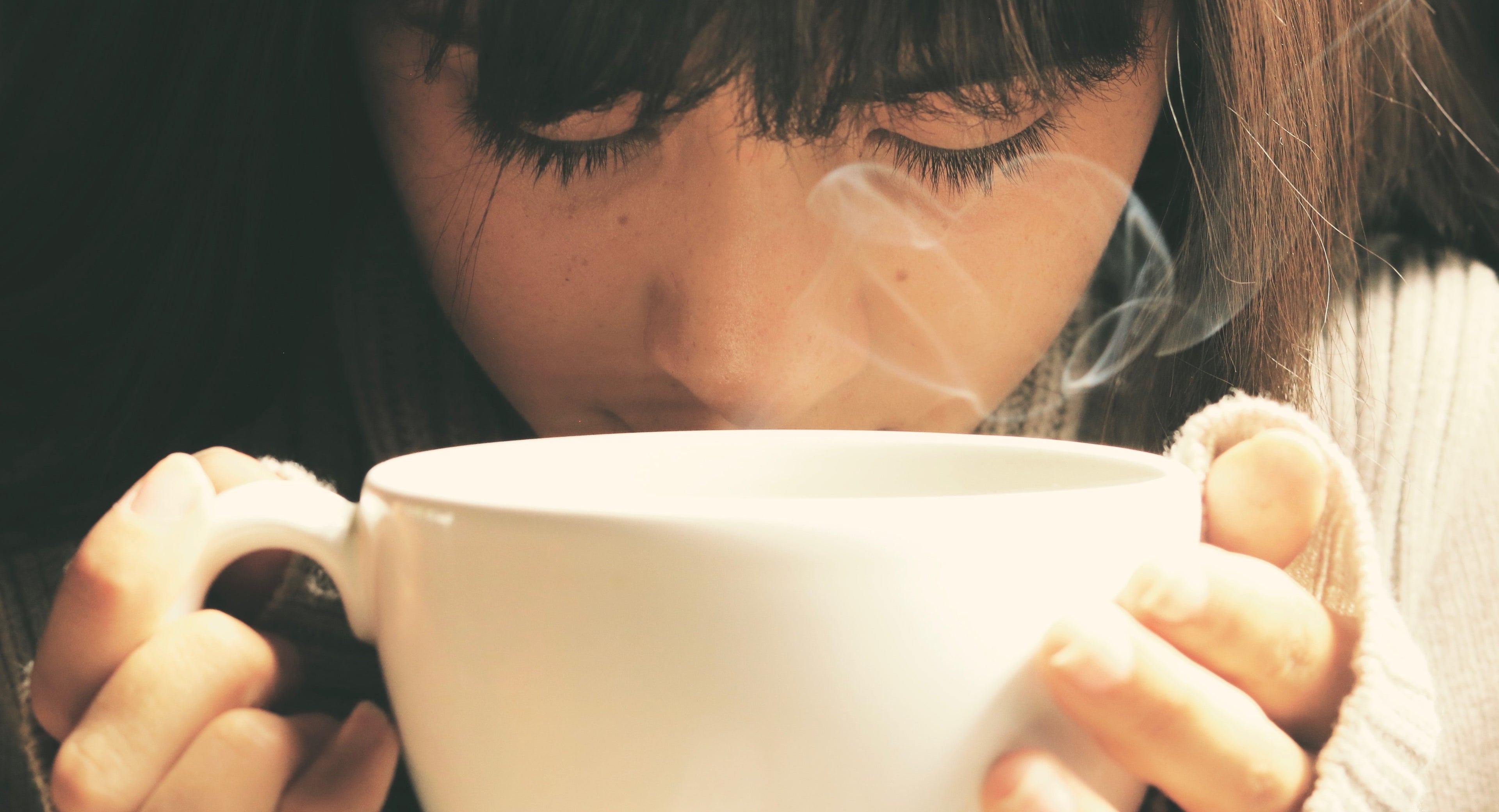 close up of woman smelling coffee in cup
